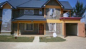 A two-story house with a stone facade, a tiled roof, and a front porch. - Elgon Village Guest House (Eldoret)