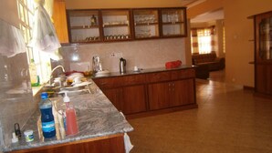A kitchen with wooden cabinets, a marble countertop, and a built-in glass display case. - Elgon Village Guest House (Eldoret)