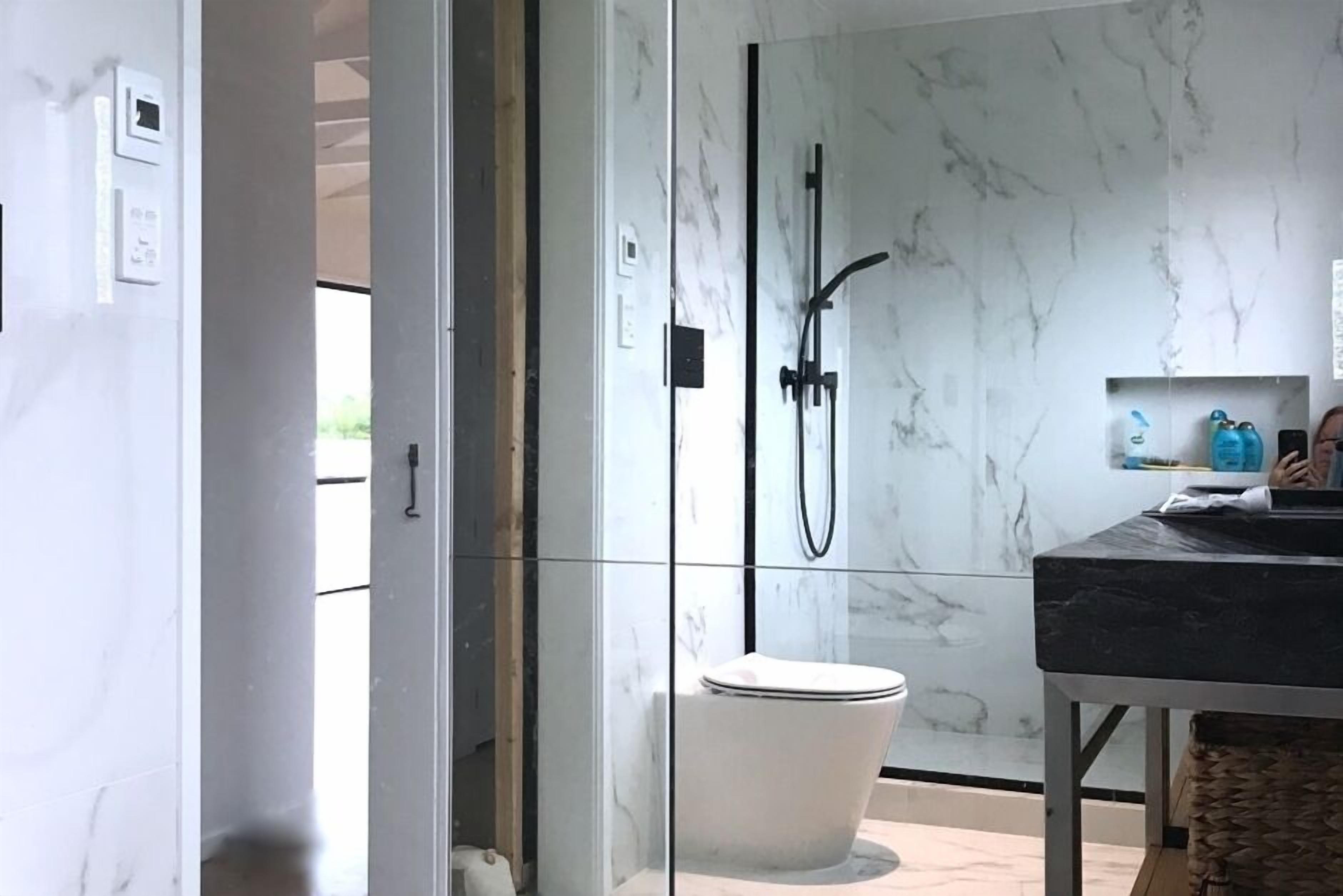 Une salle de bain moderne avec une douche à l’italienne en verre, des toilettes blanches et un pare-baignoire en marbre.