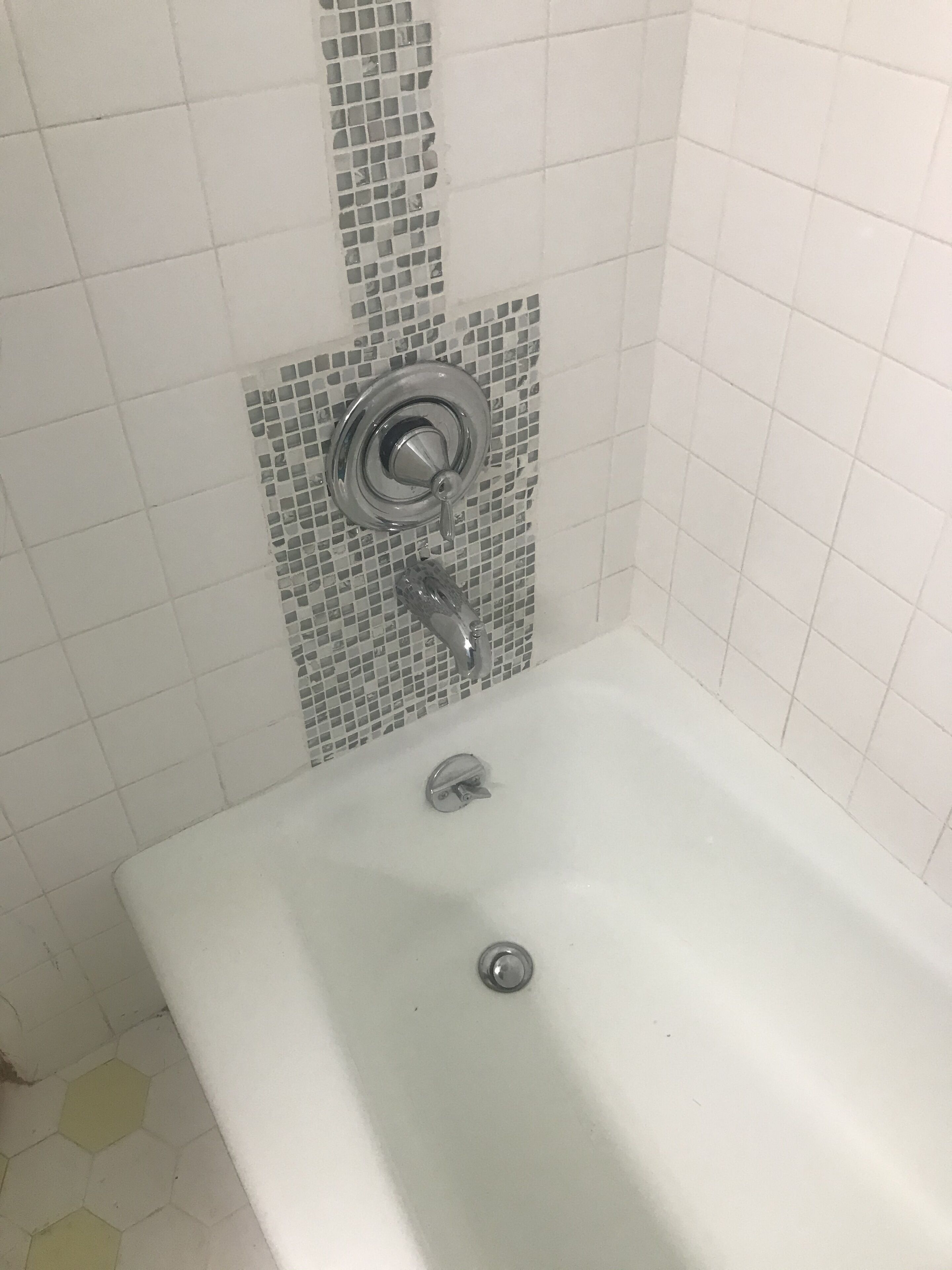 Une salle de bain avec une baignoire blanche, une douche dotée d’une porte en verre et un mur recouvert de mosaïques.