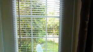 Puerta con persianas horizontales, un picaporte visible y una vista de un área exterior verde con una silla.