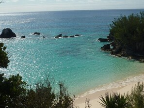 A coastal landscape with clear turquoise waters, rocky outcrops, and a sandy beach.