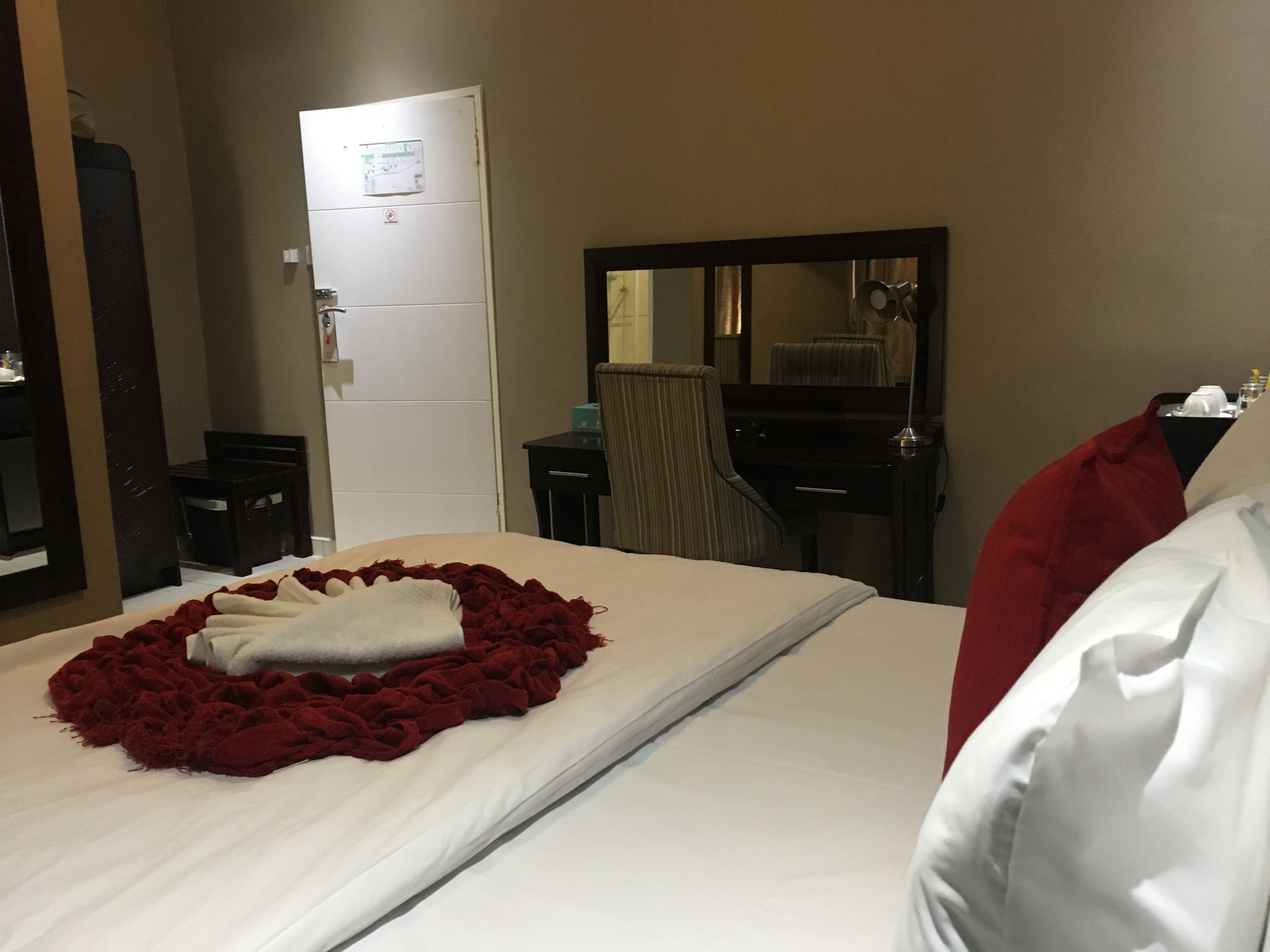 A hotel room with a bed, a dresser, a mirror, and a door.