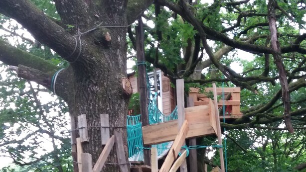 A wooden treehouse with a spiral staircase and a rope bridge.