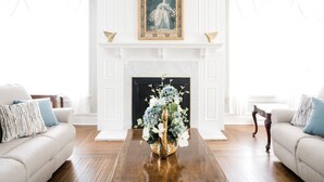 A living room with a fireplace, two sofas, and a coffee table with a floral arrangement. - Gorgeous Estate set in beautiful Lancaster County  (Bird in Hand)
