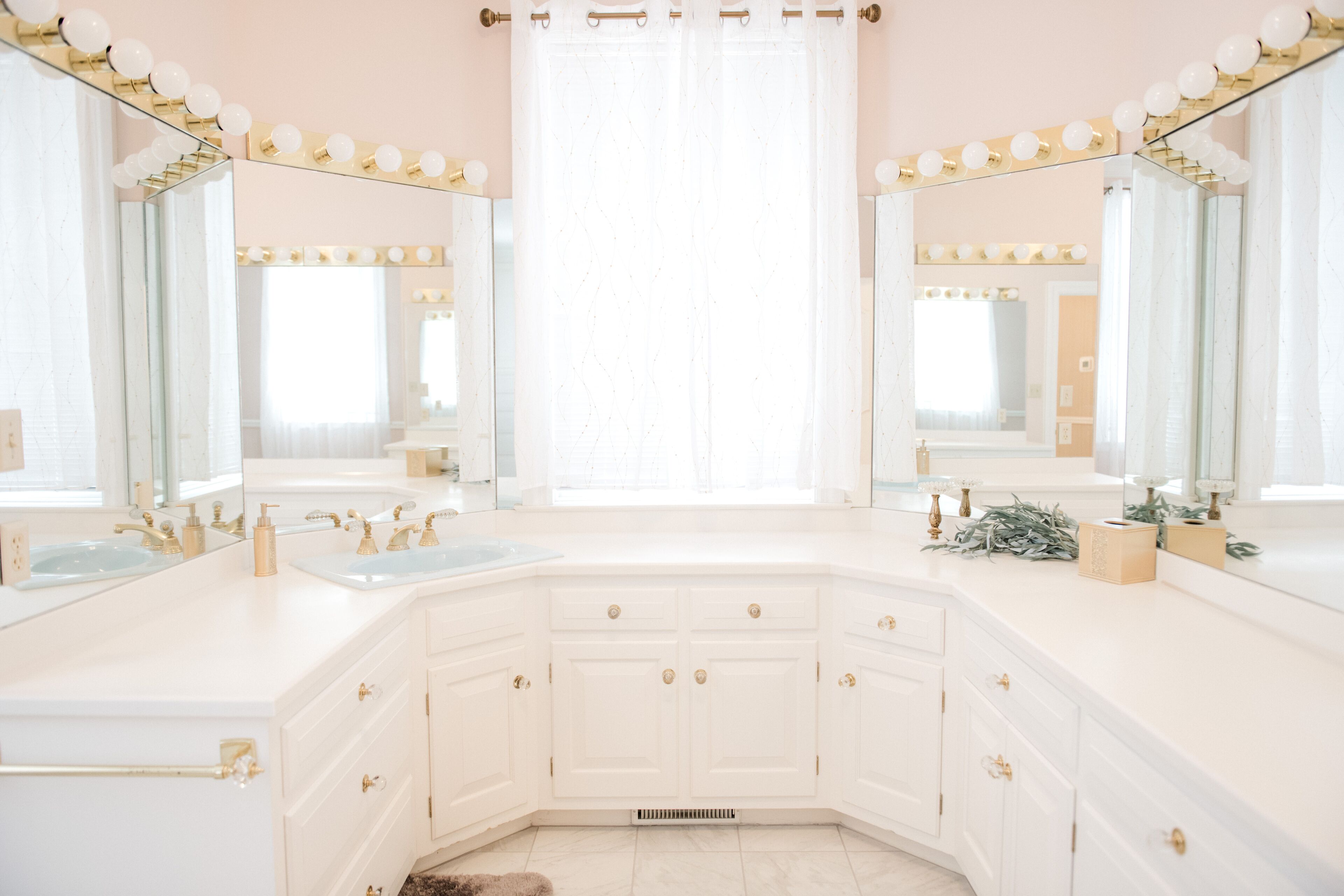 A bathroom with two sinks, a vanity, and a large mirror with lights.