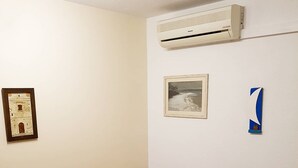 Ein Wohnzimmer mit einem roten Sofa, zwei gelben Kissen, einem gerahmten Bild, einer Klimaanlage und einer kleinen dekorativen Zahl 1.