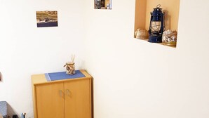 Ein Zimmer mit einem Holzkasten, einer blauen Matte darauf, einem kleinen Regal mit einer Laterne und Gläsern sowie einem Bild an der Wand.