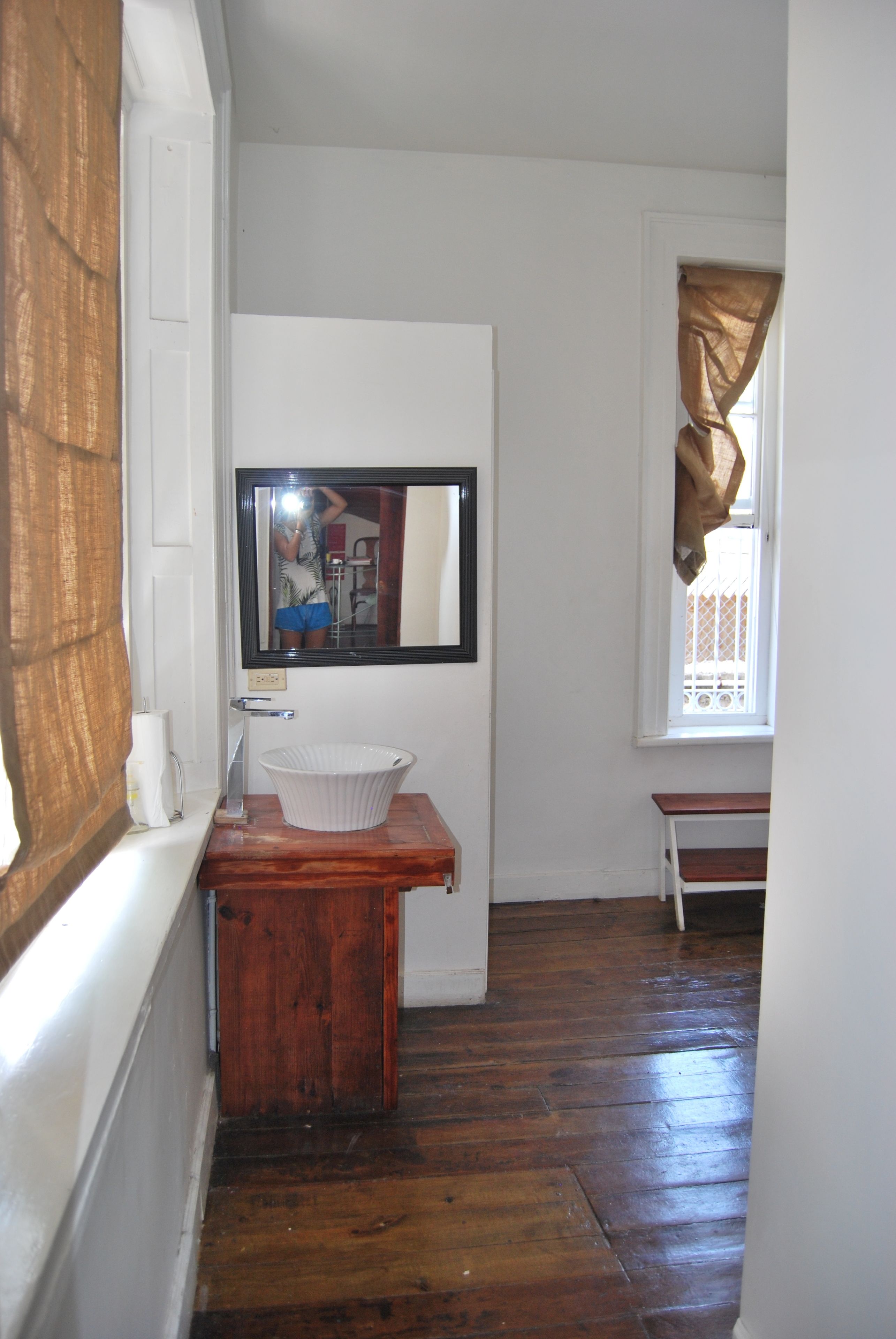A bathroom with a wooden vanity, a white sink, a mirror, and a window with a view of a fence.
