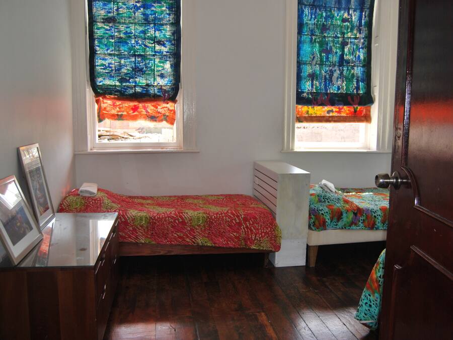 Une petite chambre avec deux lits, une commode en bois et une fenêtre ornée de rideaux colorés.