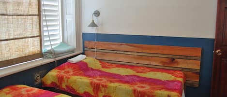 Ein Schlafzimmer mit zwei Betten, einem Fenster mit Jalousien, einer Wandlampe und einem Holzkopfstück.