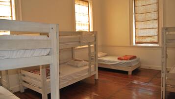 A room with bunk beds, wooden flooring, and windows with curtains.