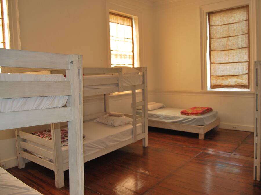 A room with bunk beds, wooden flooring, and windows with curtains.