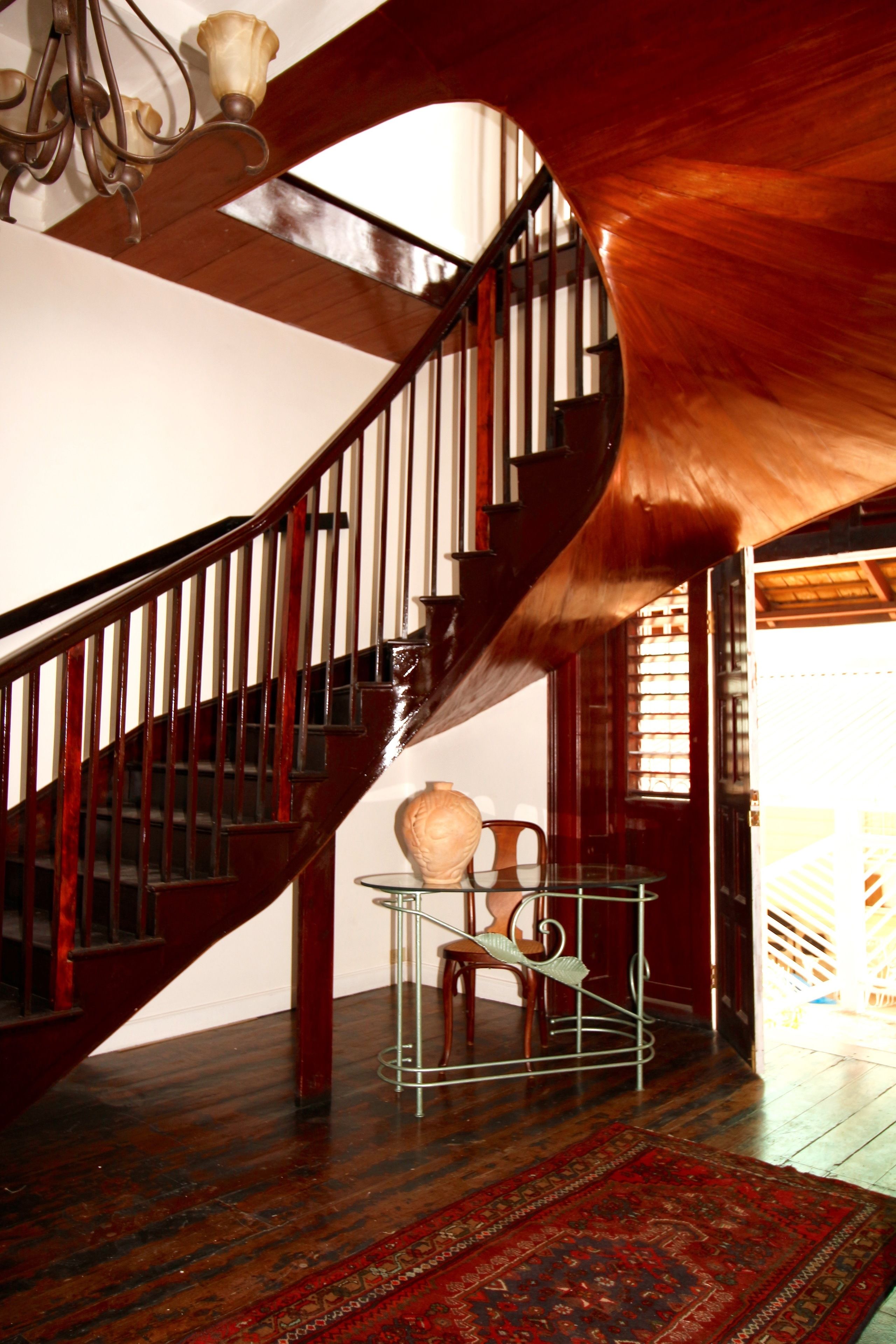 Una escalera espiral de madera con una mesa y sillas de vidrio al frente.