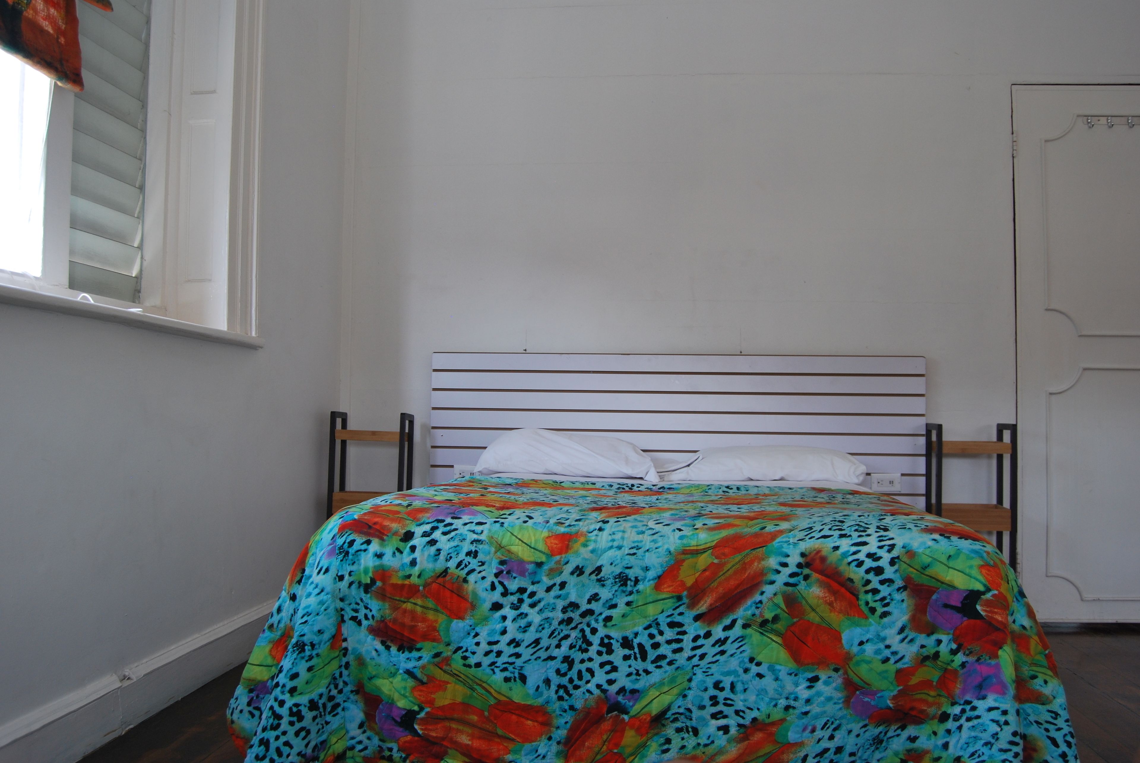 A bed with a colorful floral bedspread, a white pillow, and a wooden headboard.