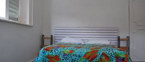 A bed with a colorful floral bedspread, a white pillow, and a wooden headboard.