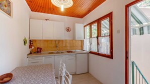 A compact kitchen with white cabinets, a tiled backsplash, and a window with lace curtains. - Pet-Friendly Studio for Two (Veli Lošinj)