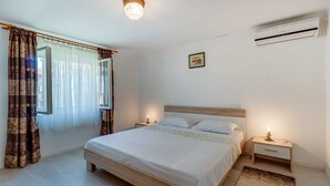 A bedroom with a bed, bedside tables, an air conditioner, a window with curtains, and a wall-mounted picture. - Pet-Friendly Studio for Two (Veli Lošinj)