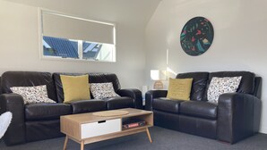 A living room with two black leather sofas, a wooden coffee table, and a wall-mounted round painting. - Heart of Russell Apartment - Russell Apartment (Russell)