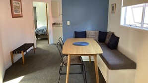 A compact living space with a wooden table, bench, and sofa. A door leads to another room with a bed. - Heart of Russell Apartment - Russell Apartment (Russell)