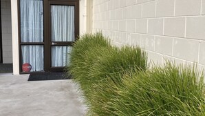 A building with a brick wall, a door with curtains, and a small garden area. - Heart of Russell Apartment - Russell Apartment (Russell)