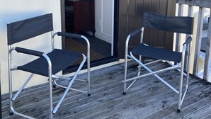 Two foldable chairs on a wooden deck with a view of a building's interior through an open door. - Heart of Russell Apartment - Russell Apartment (Russell)