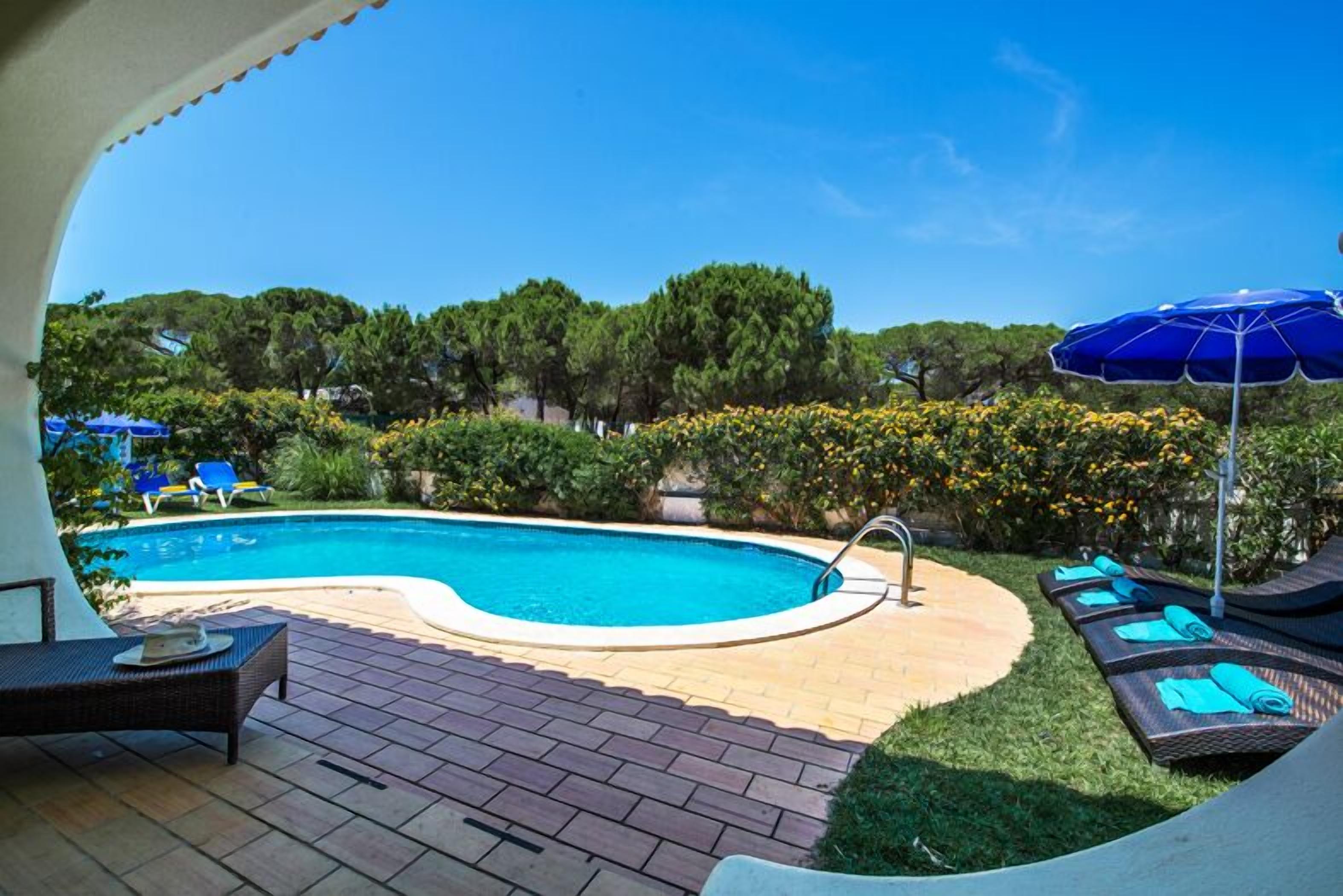 Ein Swimmingpool mit Liegestühlen und Sonnenschirmen, umgeben von Grünpflanzen und Bäumen.