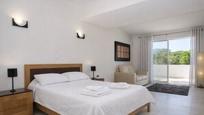 Un dormitorio moderno con una cama grande, mesitas de noche, una silla y vistas al verdor a través de la ventana.