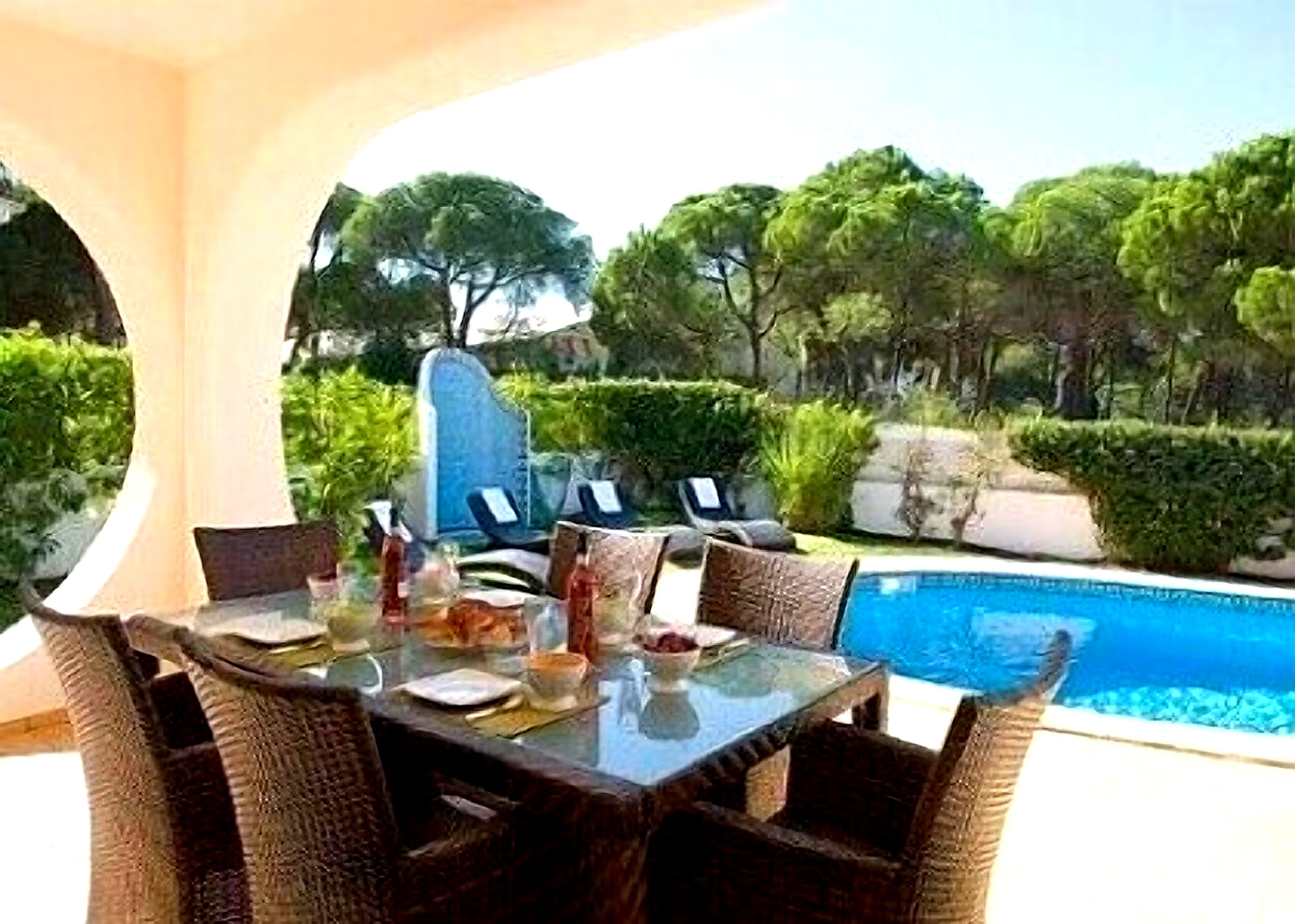 Ein Tisch mit Glasplatte, Korbstühle, eine Steinskulptur und Blick auf den Pool.