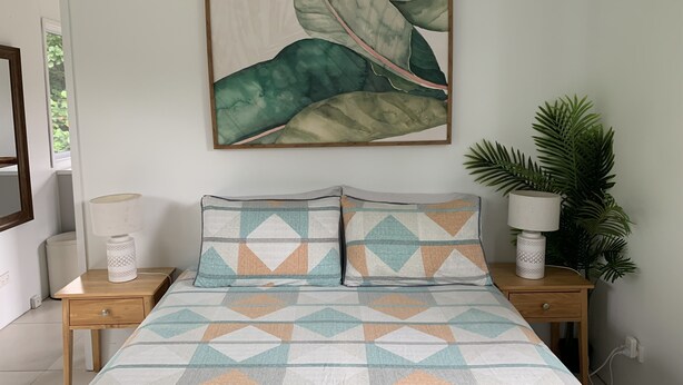A bedroom with a bed, two nightstands, a wall-mounted painting, and a potted plant. - Cosy and Modern Studio in Muri Beach (Muri Beach)