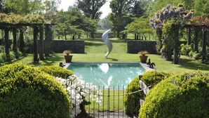 A well-maintained garden with a swimming pool, surrounded by neatly trimmed hedges and a stone wall.