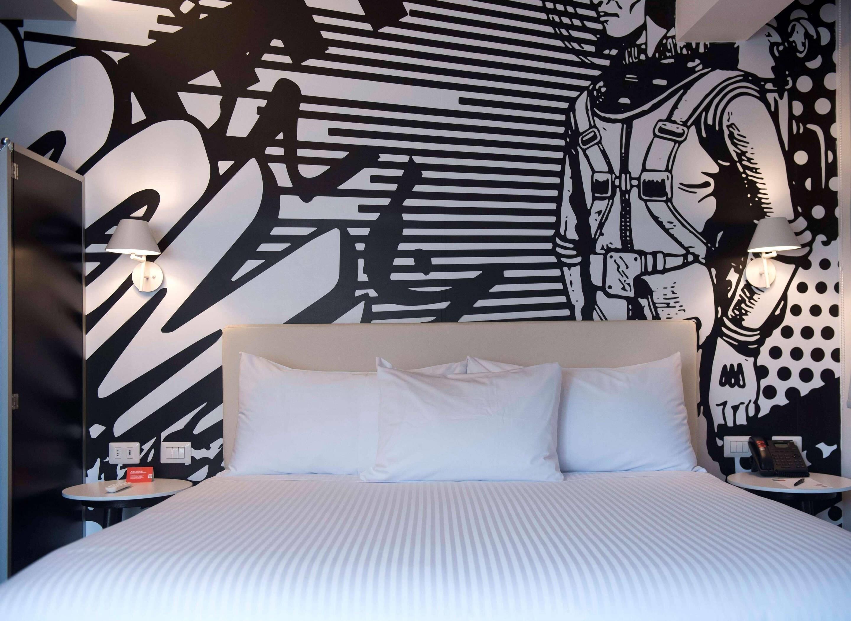 A hotel room with a large bed, two bedside lamps, a wall with abstract art, and a telephone on the nightstand.