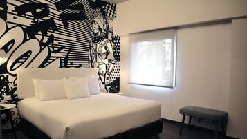 A modern hotel room with a large bed, a bench, a wall mural, and a window.