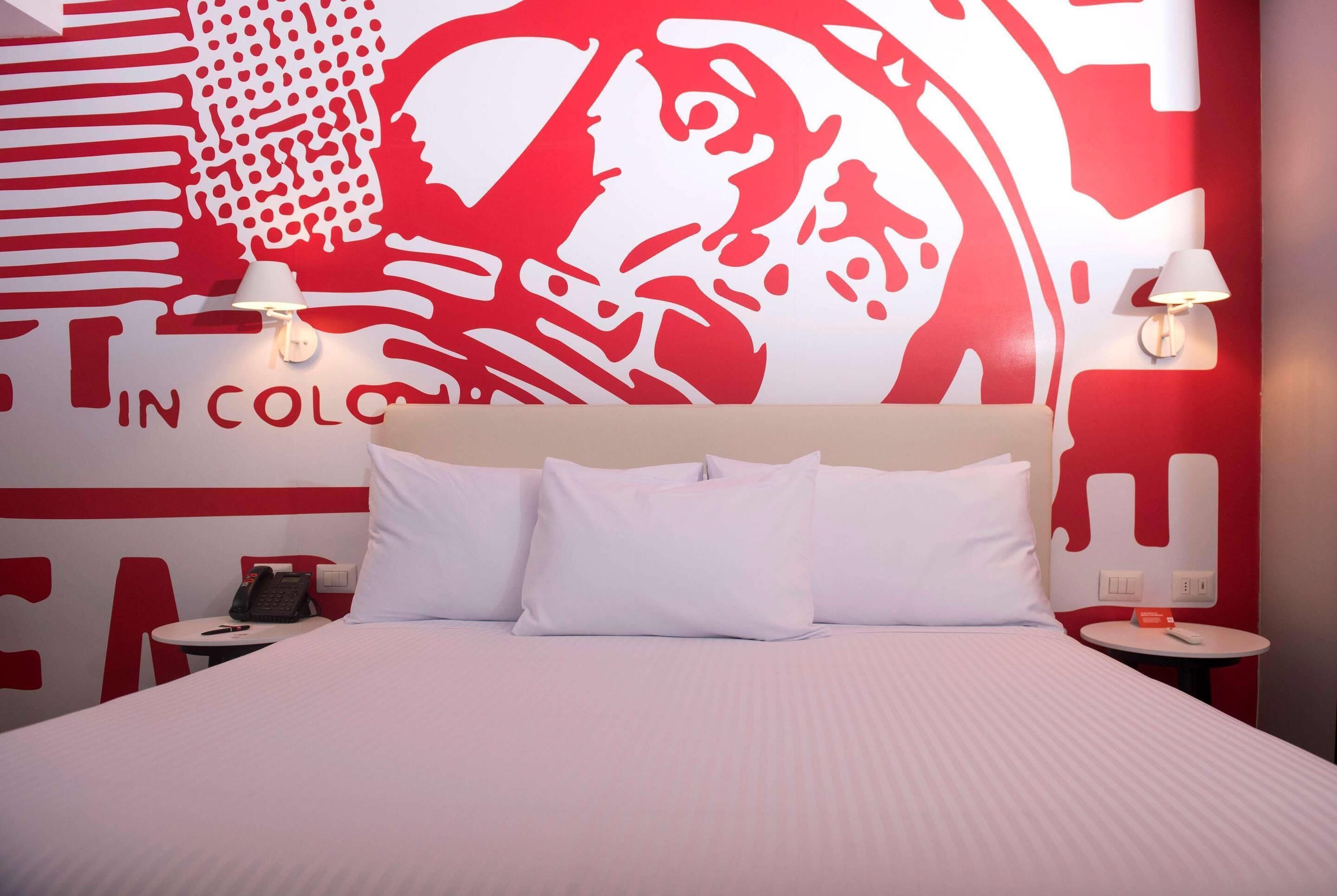 A hotel room with a large bed, two bedside tables, a telephone, and a wall with a red and white abstract design.
