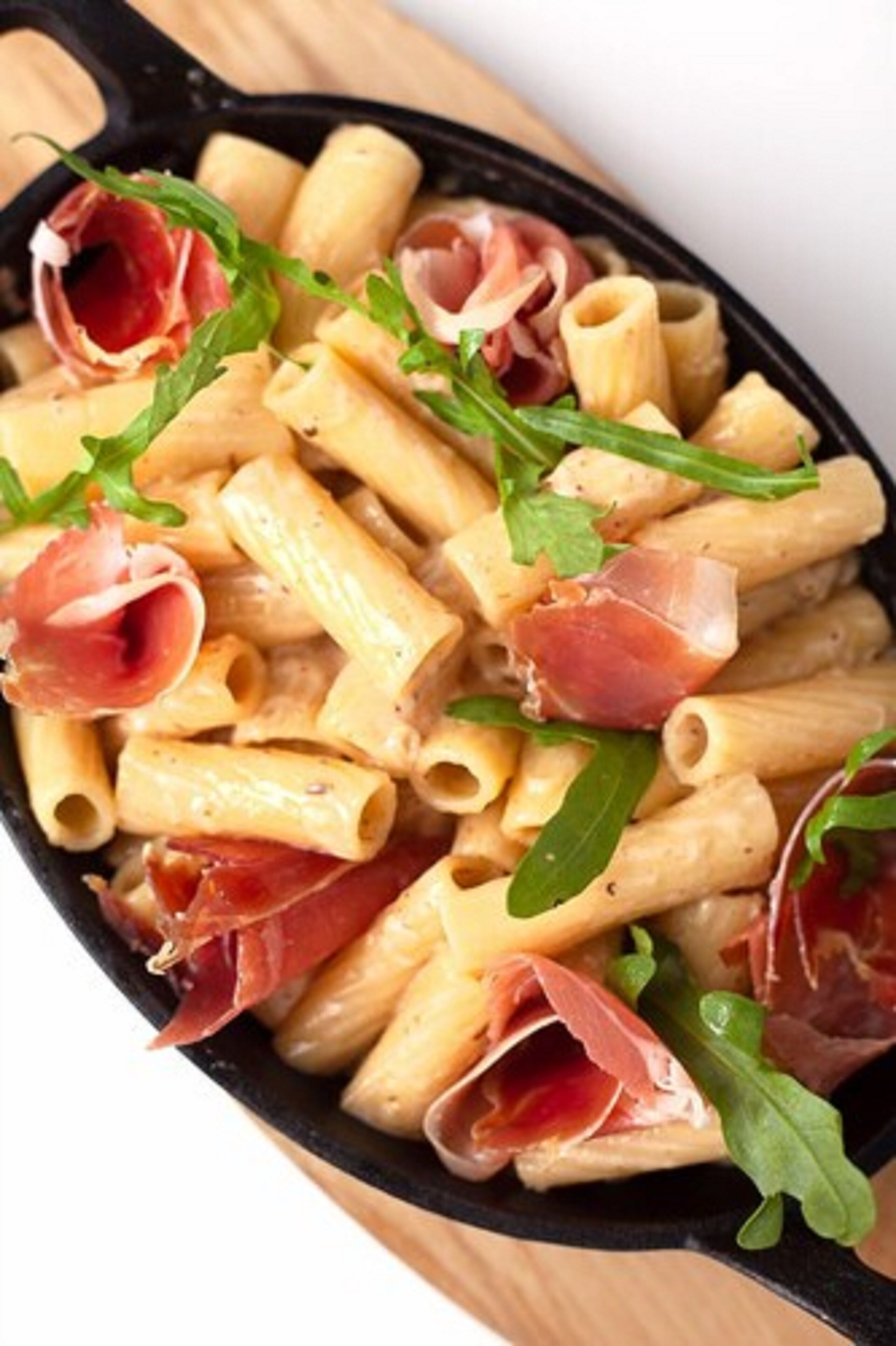 A skillet with pasta, prosciutto, and arugula.