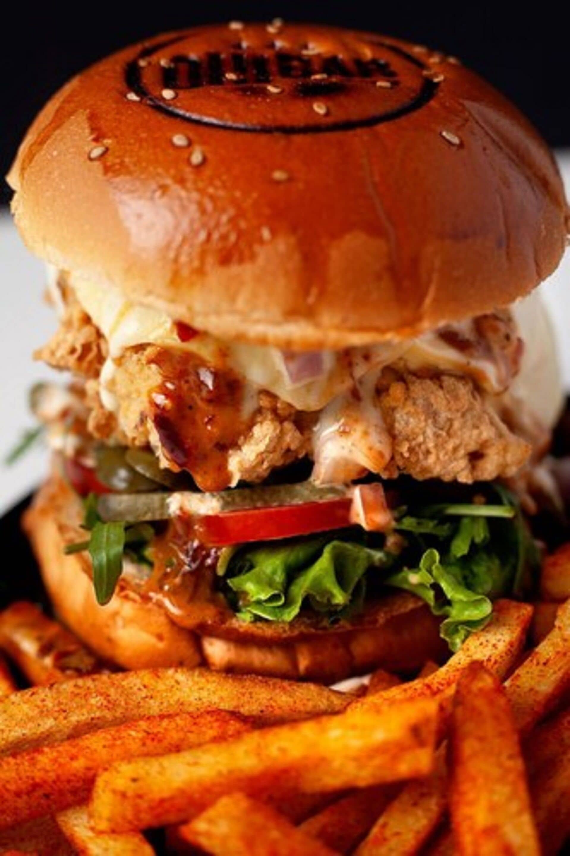Hamburguesa con pan de sésamo, lechuga, tomate y una crujiente hamburguesa de pollo, acompañada de papas fritas.