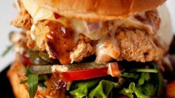 Hamburguesa con pan de sésamo, lechuga, tomate y una crujiente hamburguesa de pollo, acompañada de papas fritas.