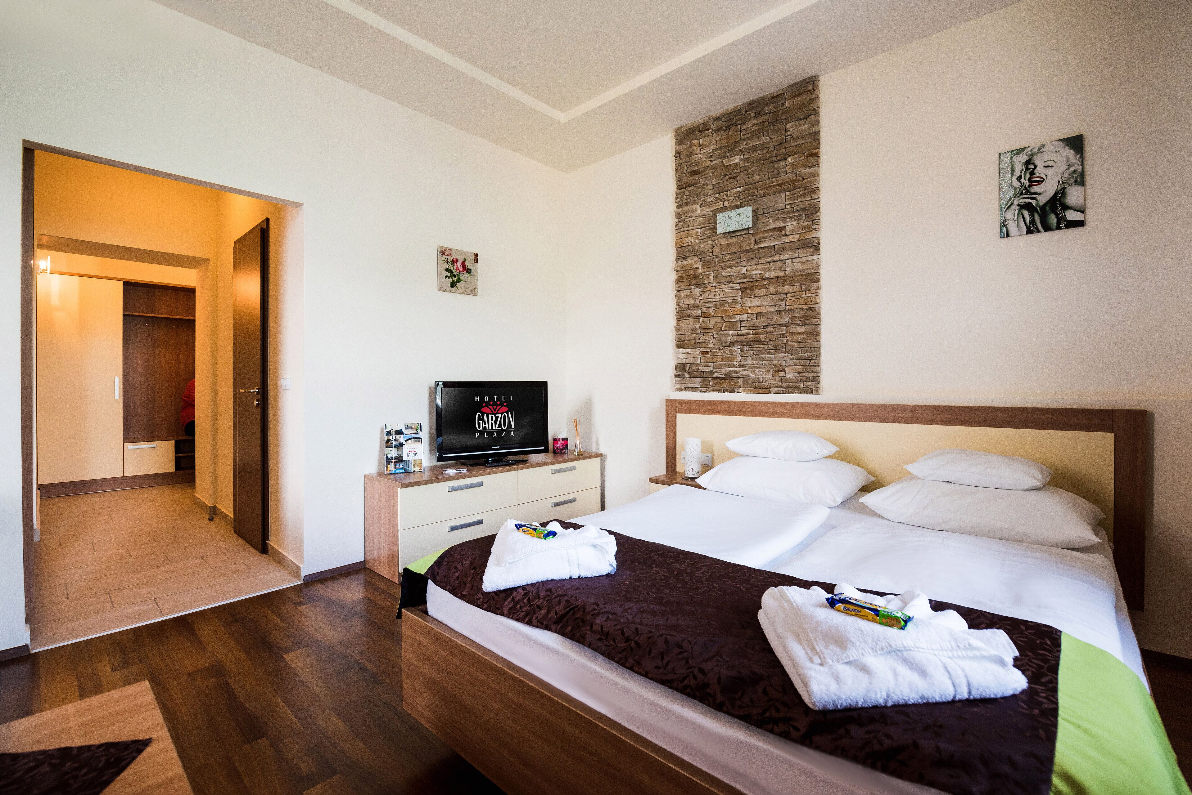Ein Hotelzimmer mit Holzboden, einem Bett mit weißer und brauner Bettwäsche, einem Fernseher auf einem Nachttisch aus Holz und einer Wand mit Ziegeln.
