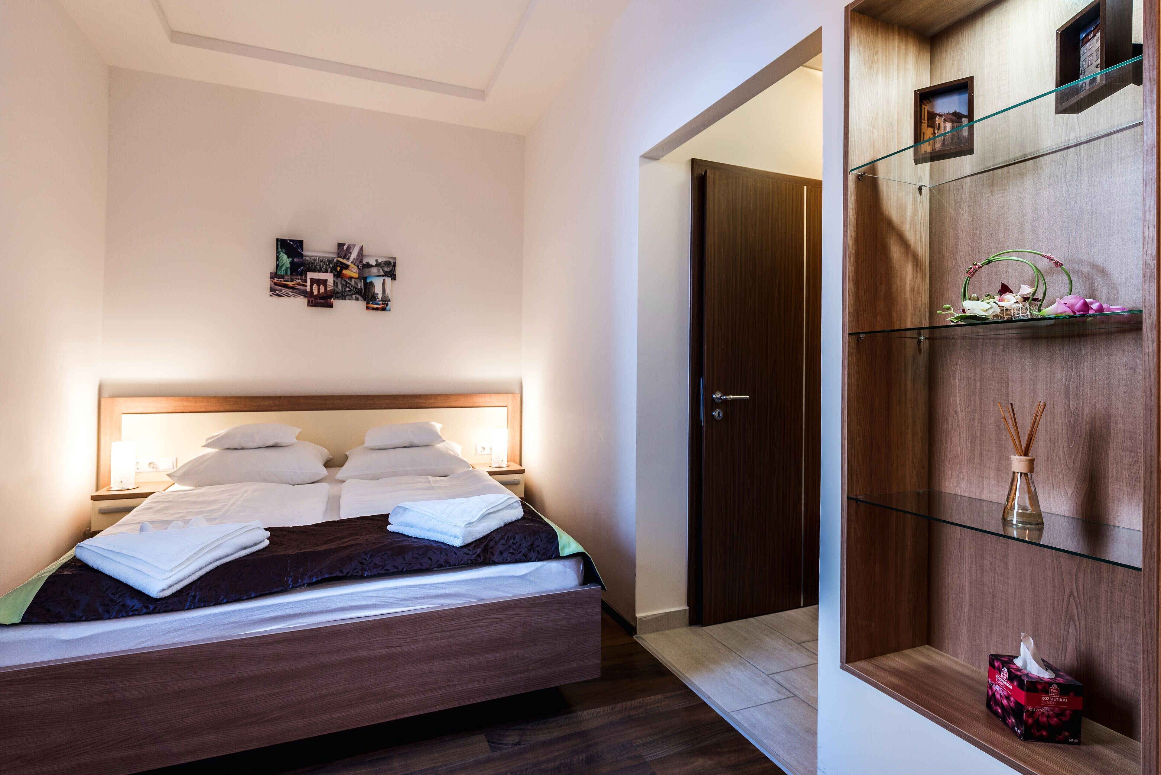 Cama bem arrumada com cabeceira de madeira, mesa de cabeceira com abajur e uma colagem de fotos na parede.