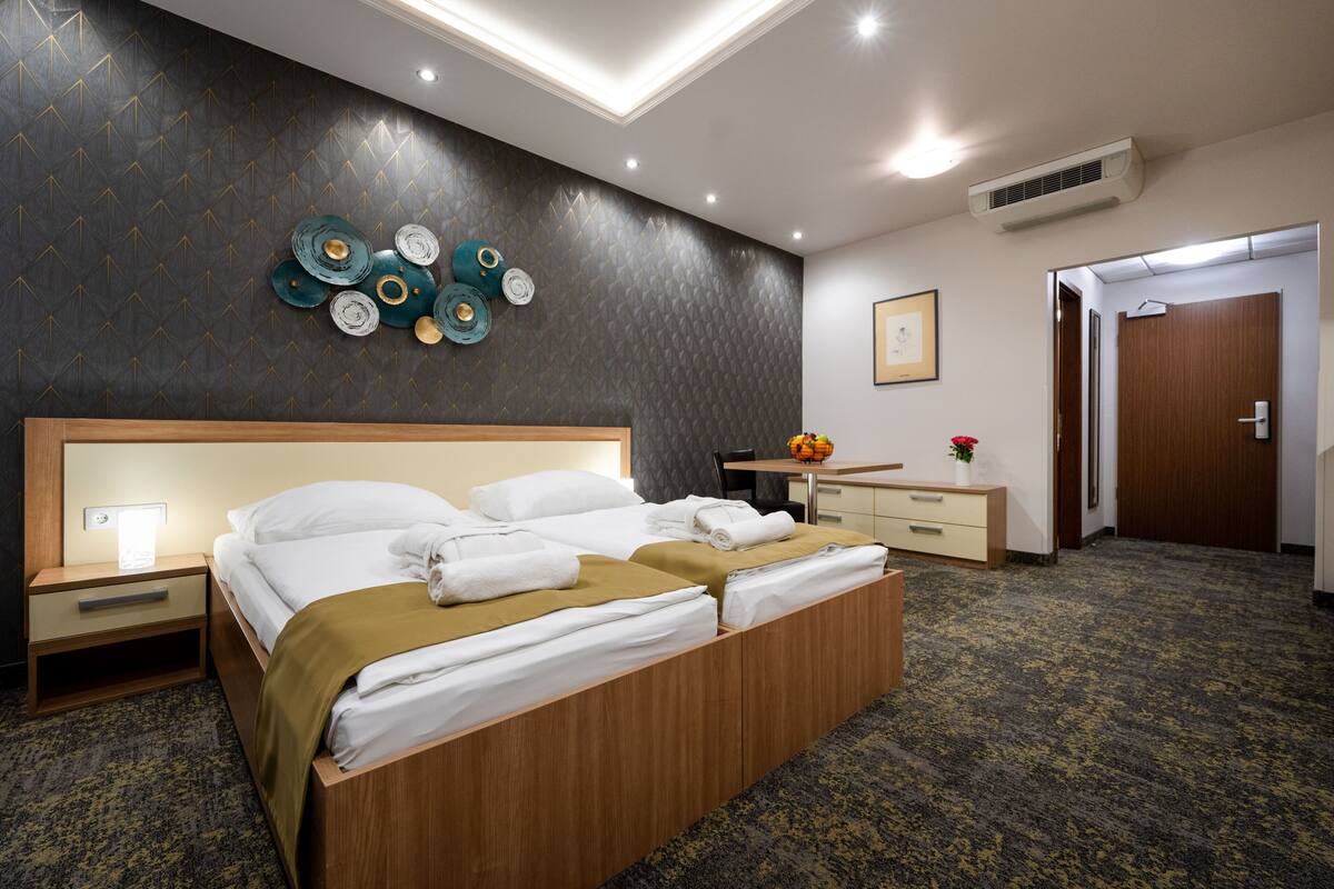 Une chambre d’hôtel comprenant un lit, des tables de chevet, un bureau, une chaise, une petite table avec un vase et une porte.