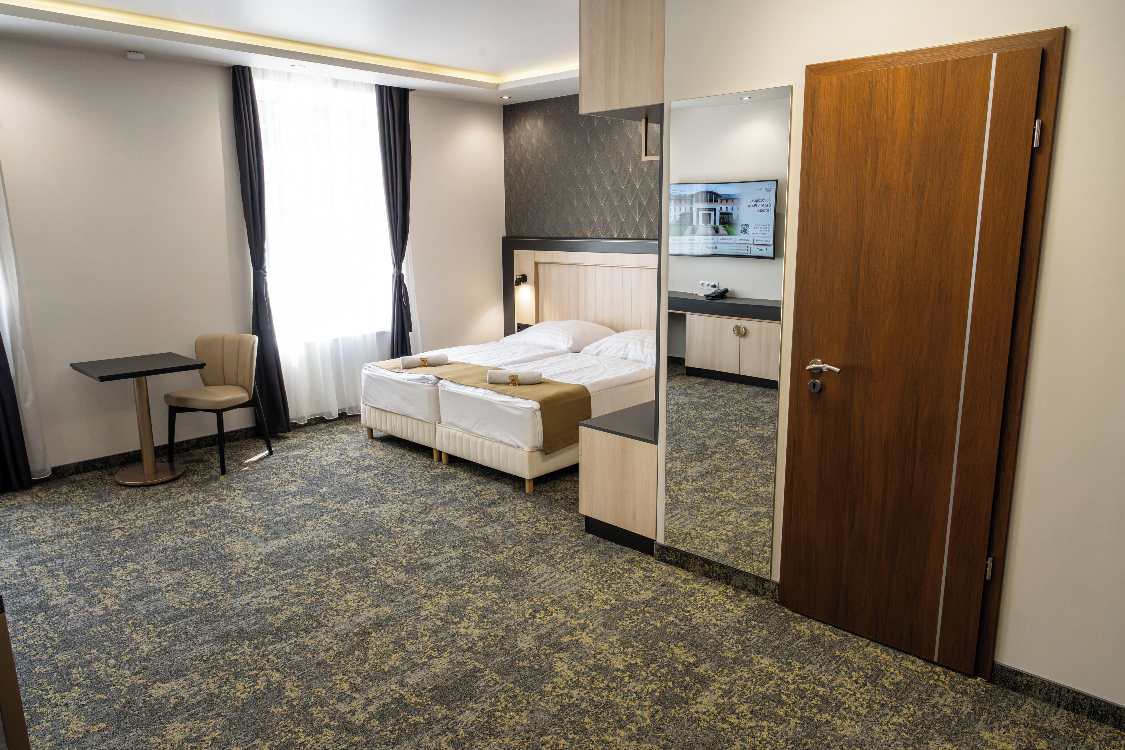 Una habitación de hotel con una cama, un escritorio, una silla, un espejo y una puerta.