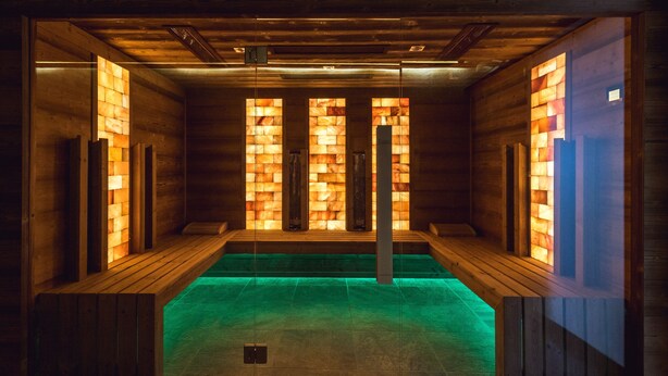 Eine Sauna mit Holzwänden und einem grünen Boden, mit einer zentralen Säule und Bänken entlang der Seiten.