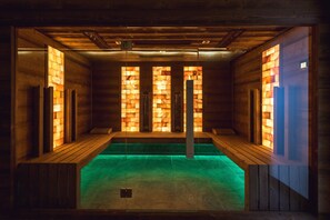 A sauna with wooden walls and a green floor, featuring a central pillar and benches along the sides. - Garzon Pláza (Gyor)