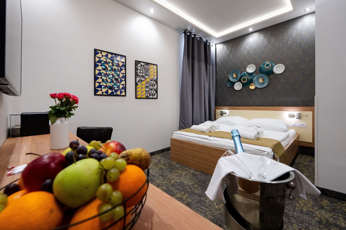 Une chambre d’hôtel avec un lit, un bureau sur lequel se trouvent des fruits, un vase rempli de fleurs et des œuvres d’art accrochées au mur.