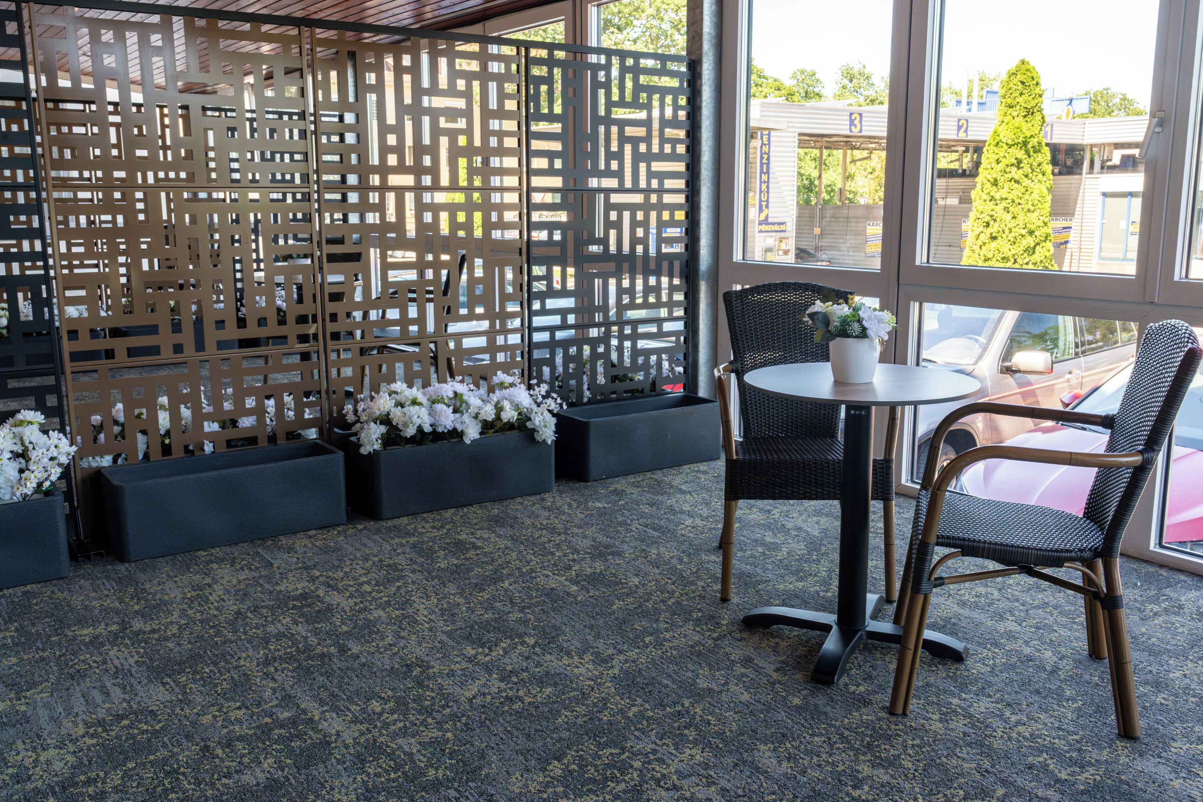 Un espace de détente intérieur moderne, agrémenté d'un paravent décoratif, de chaises en osier noir, d'une table ronde et de fleurs blanches dans des jardinières.