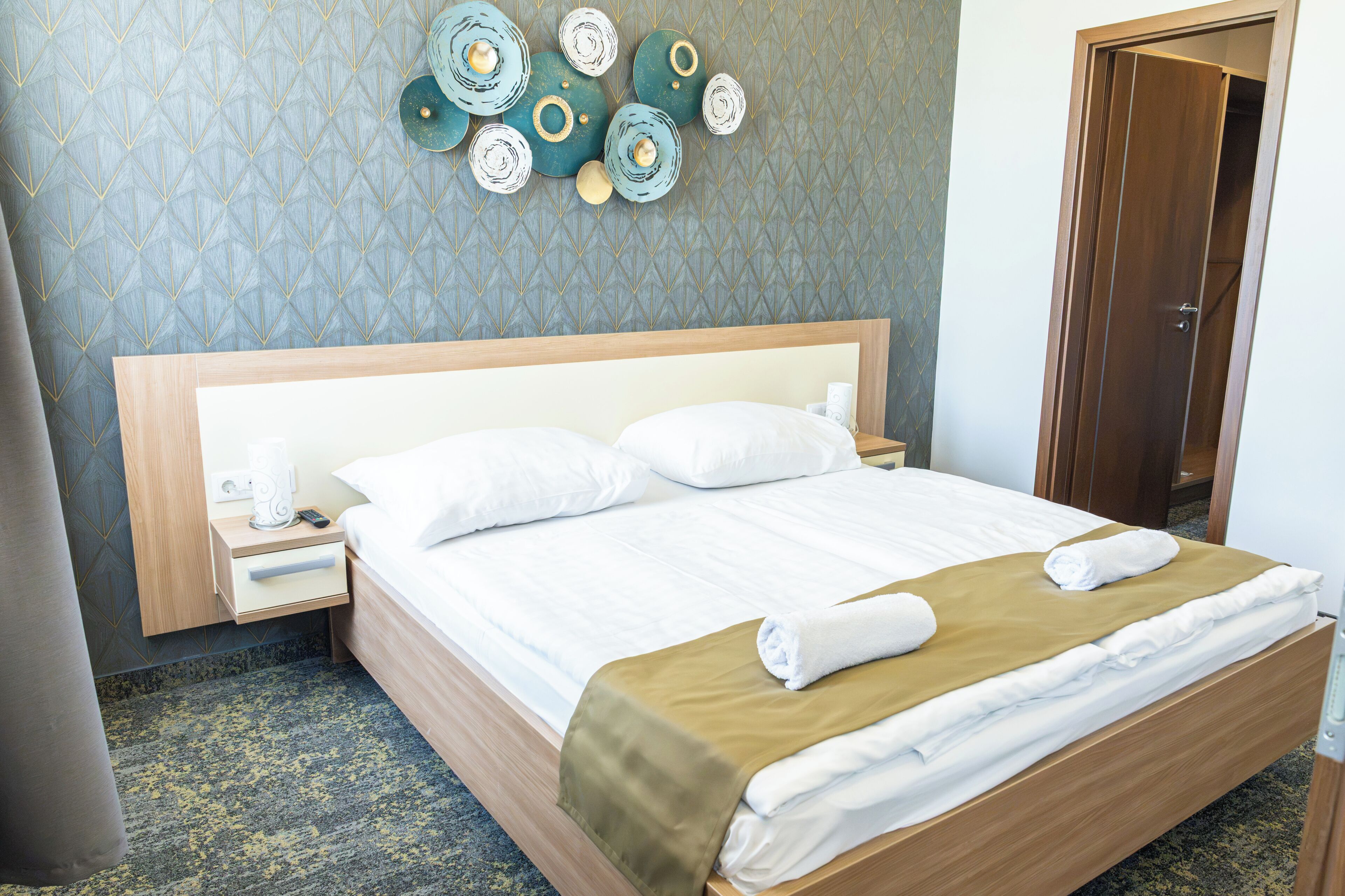 A hotel room with a bed, a nightstand, a wall clock, and a door.
