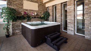 Ein Wellnessbereich mit Whirlpool, Steinwänden, Blumentöpfen und Blick ins Freie.