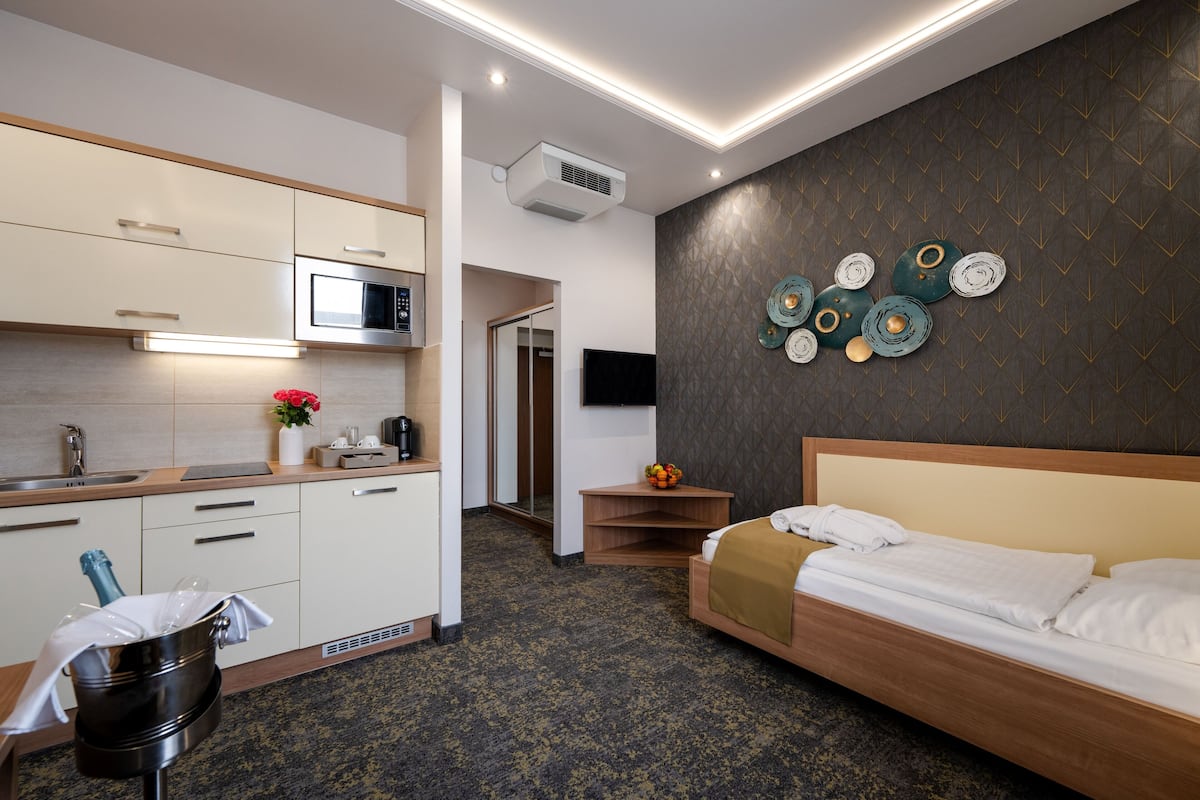 Une chambre d’hôtel compacte comprenant un coin cuisine, un lit, un téléviseur fixé au mur et une décoration murale composée d’assiettes.