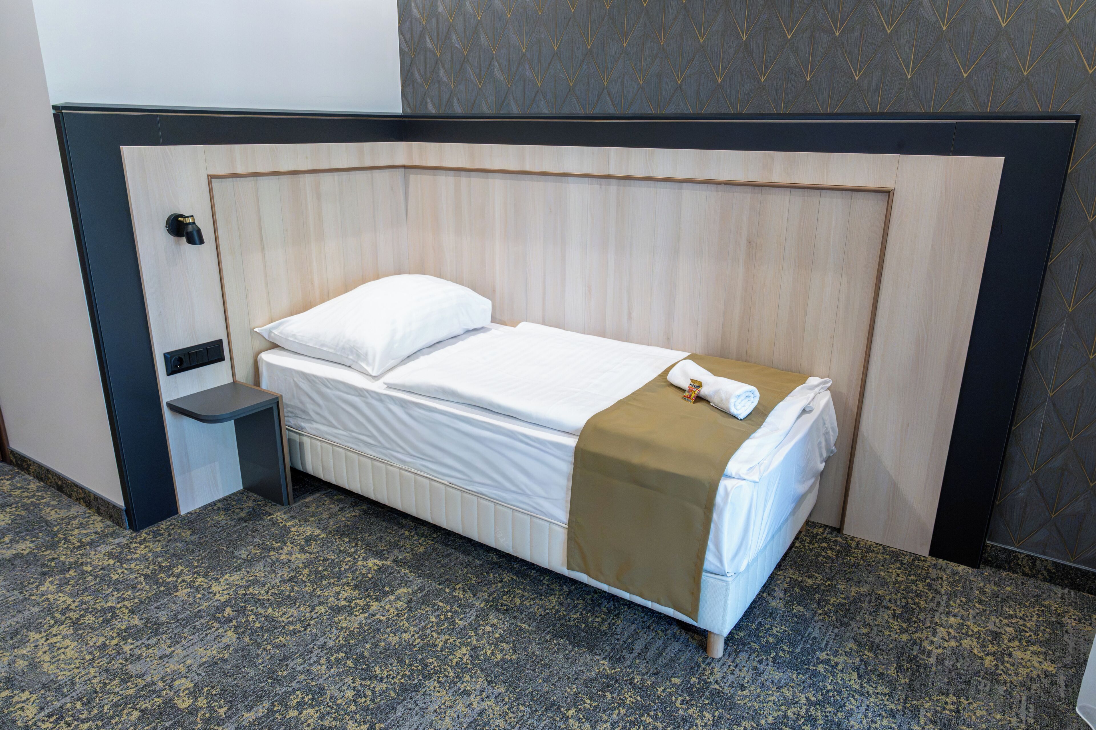 A single bed with a wooden headboard, a bedside table, and a wall with a geometric pattern.