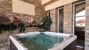 Ein Whirlpool mit Blick auf eine Steinwand, umgeben von Pflanzen und Blumen.